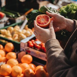 A close-up of a person holding a sliced orange at an outdoor market, showcasing fresh produce.